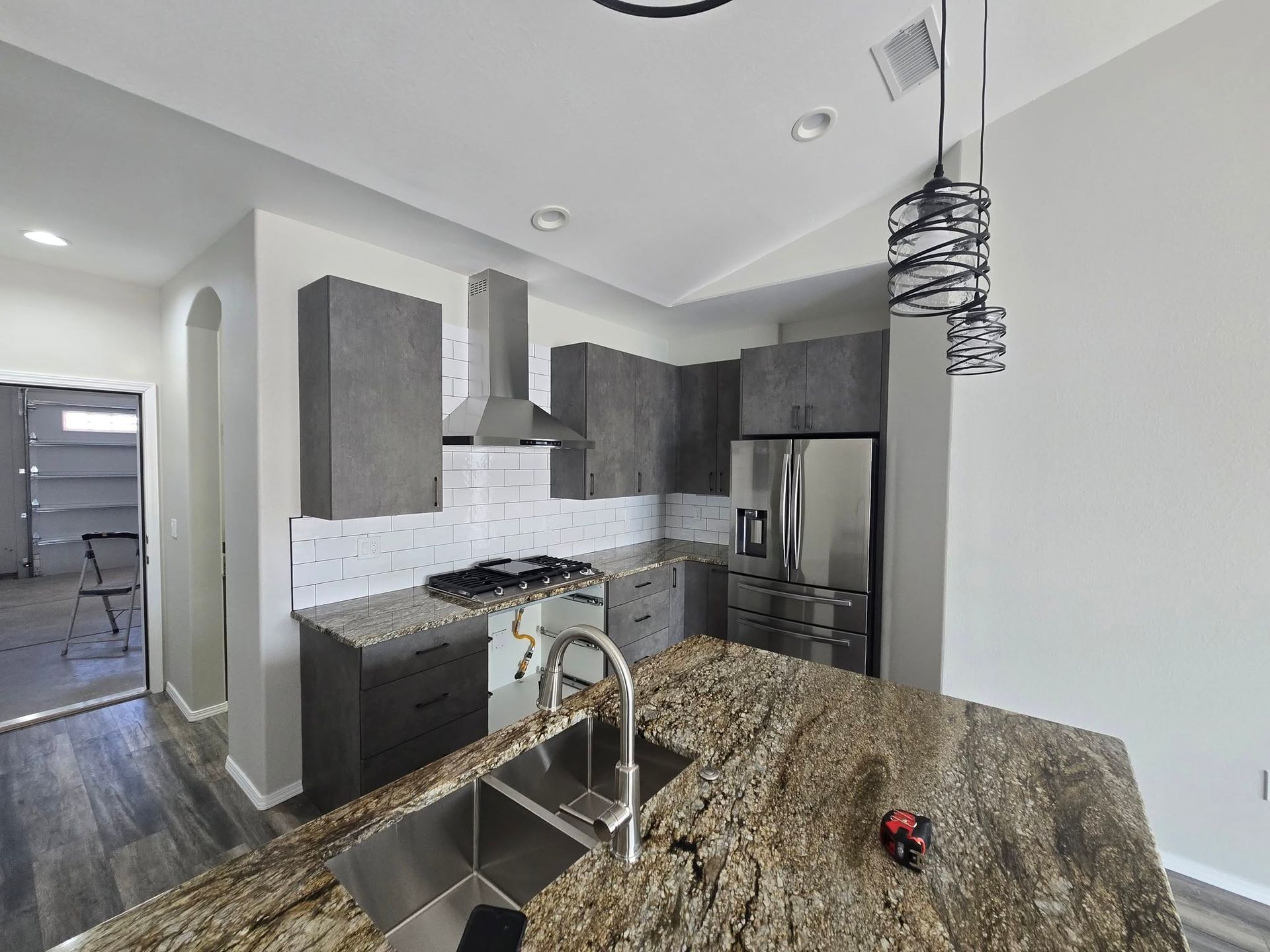 Modern kitchen with gray cabinets, stainless appliances, and a granite island sink.