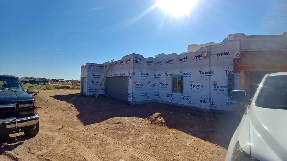Construction site with wrapped modular building, parked vehicles, and bright sun on a dirt lot