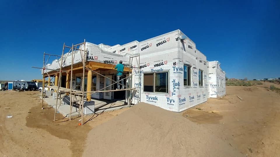 Partially built white beach house under construction on sandy lot, with scaffolding and blue sky