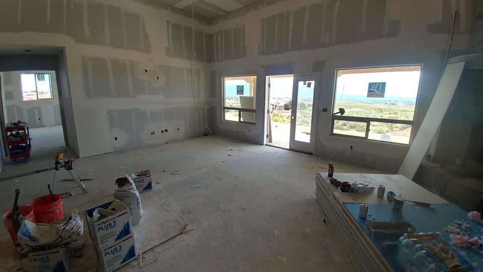 Unfinished room with drywall, construction materials, and large open windows showing an outdoor view.