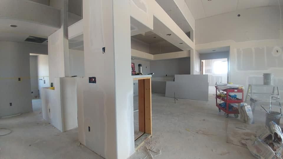 Empty unfinished room with white walls, exposed columns, and construction materials on the floor.