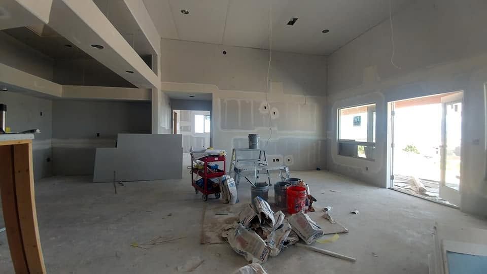 Unfinished kitchen interior with exposed drywall, construction materials, and daylight through windows and glass doors