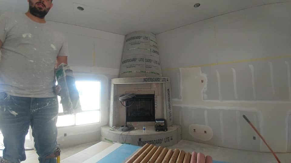 Person standing in a room under construction beside a built-in fireplace and unfinished walls