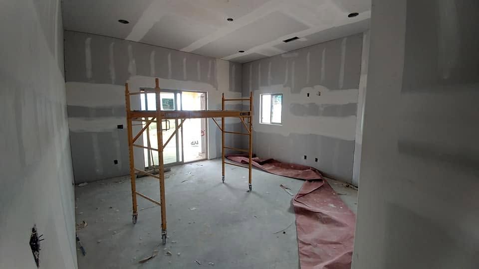 Empty room under renovation with scaffolding, unfinished walls, and a plastic-covered floor.