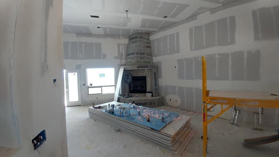 Unfinished room with drywall, a stone fireplace, scaffolding, and construction materials on the floor