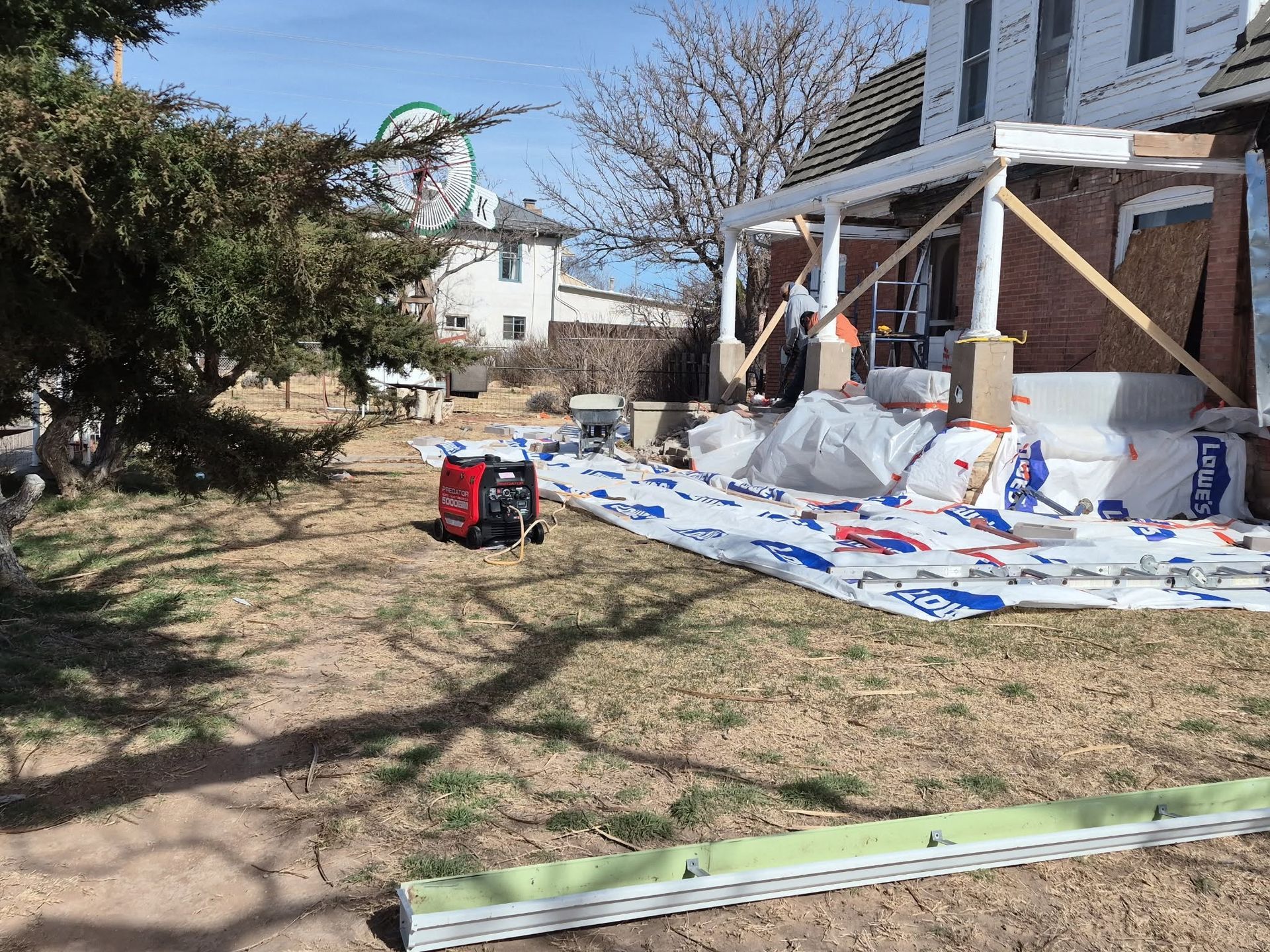 Construction supplies and tarp-covered porch beside a house, with tools scattered across the yard.
