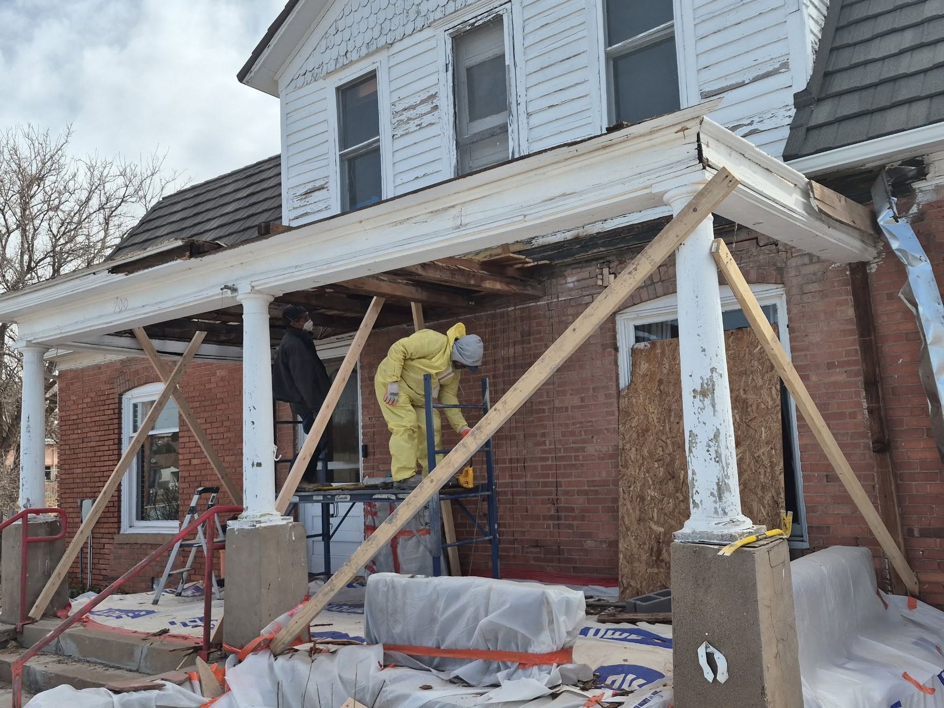 Workers rebuilding a brick house porch with white columns and scaffolding in winter