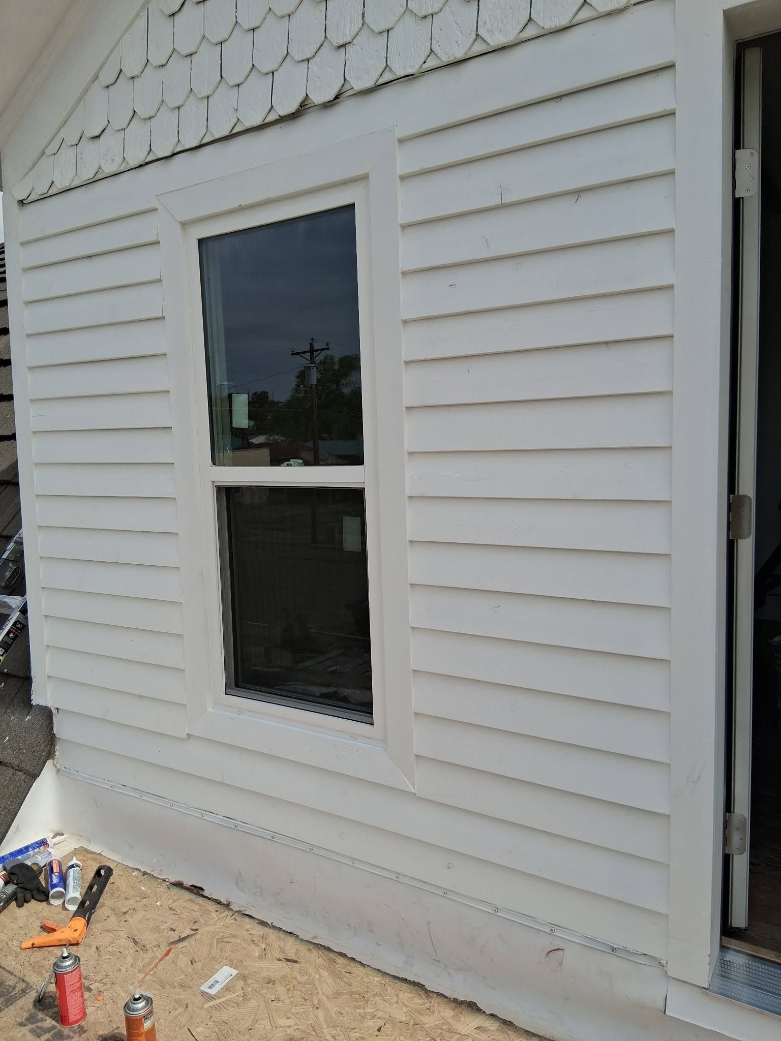 White house siding with a single window and open doorway, with construction tools and debris below