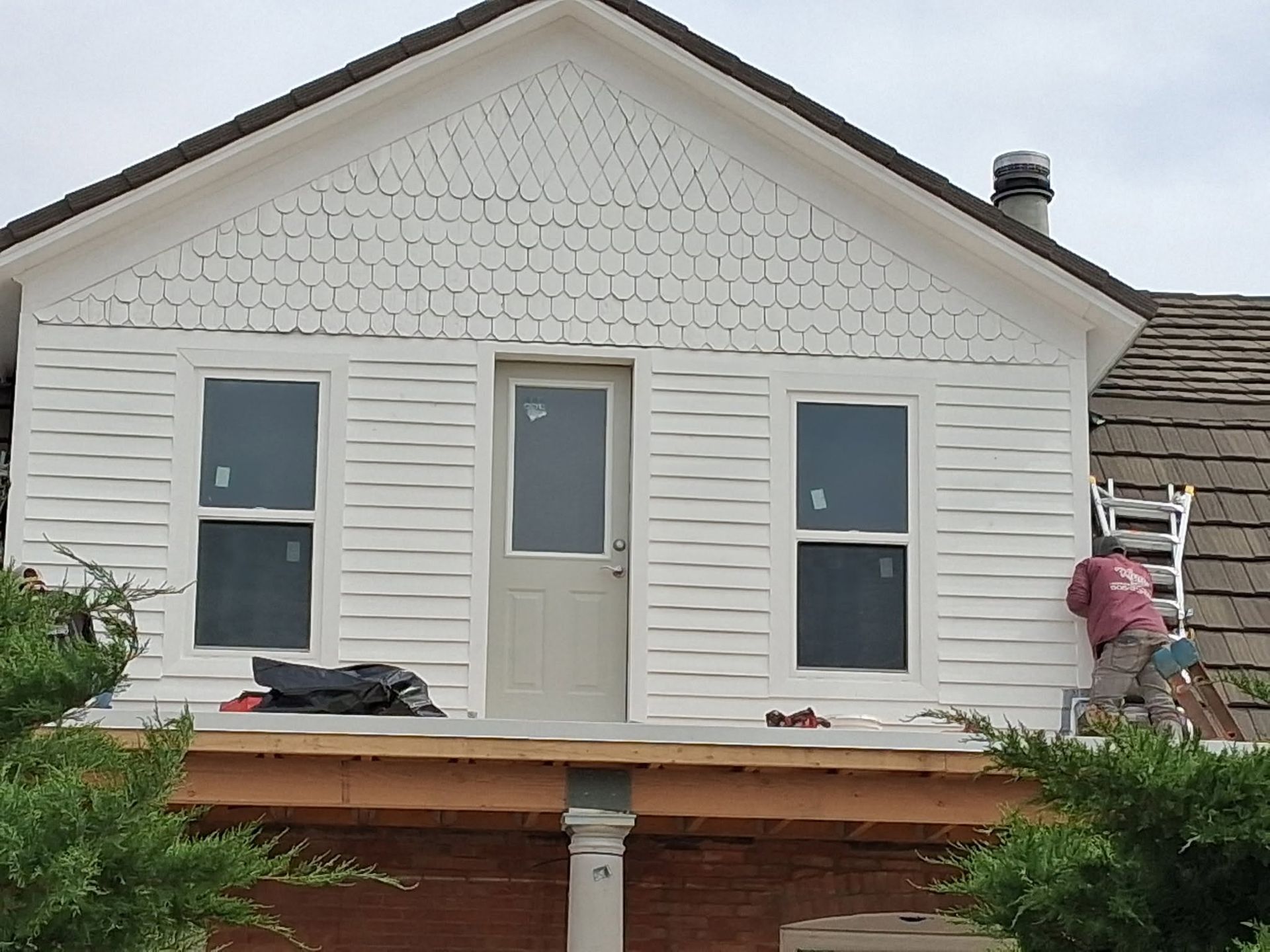 A white house front with new wood porch decking and two workers installing siding
