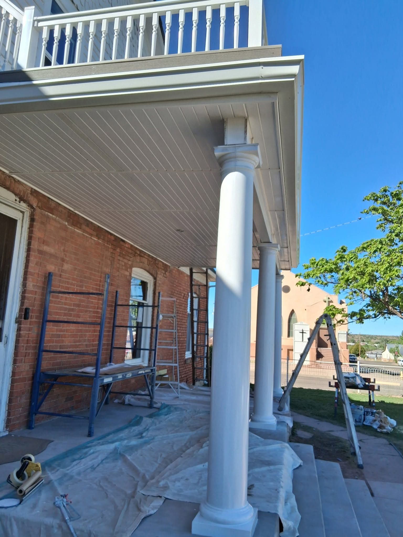 Front porch renovation with white columns, brick wall, scaffolding, and covered walkway under blue sky