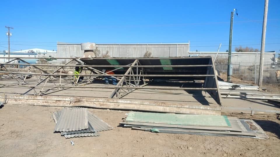 Collapsed metal structure at a dusty construction site, with workers inspecting the debris.