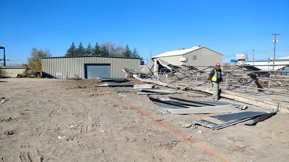 Demolition site with rubble and a worker in a high-visibility vest near damaged buildings under a clear sky