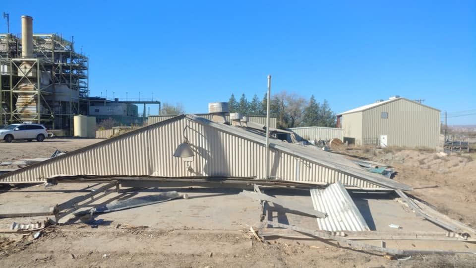 Collapsed metal structure in a dusty industrial yard under a clear blue sky