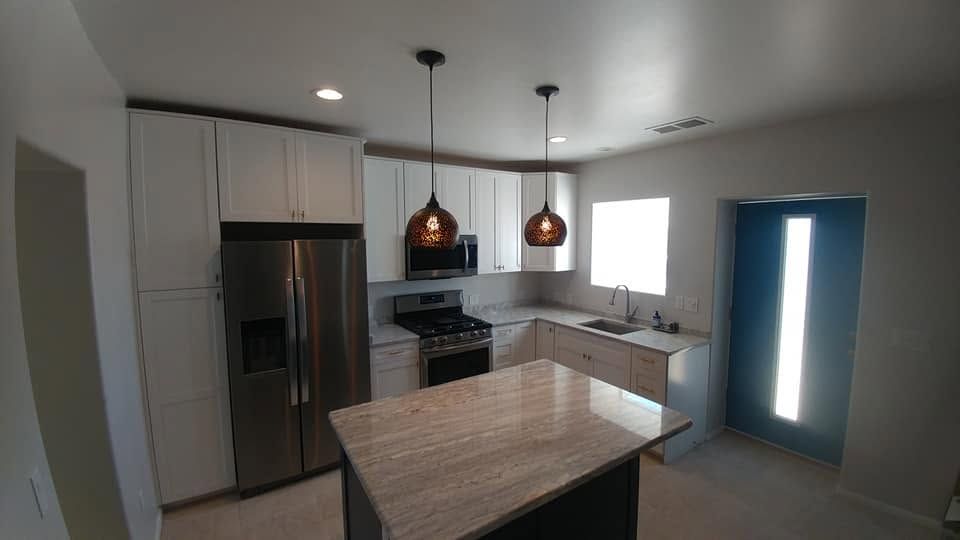 Modern kitchen with stainless steel appliances, white cabinets, island, pendant lights, and a bright doorway.