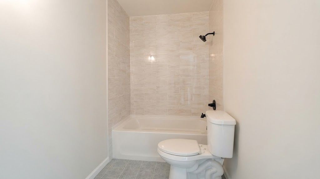 Small bathroom with a tiled shower-tub, toilet, and white walls, viewed from the doorway