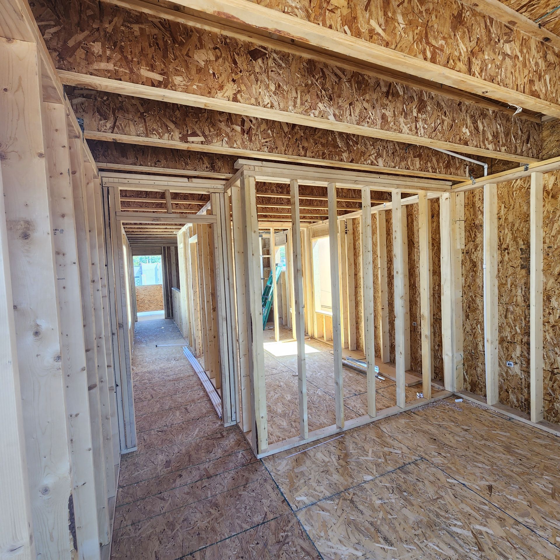 Interior of a framed house under construction, with unfinished wood studs and plywood flooring.