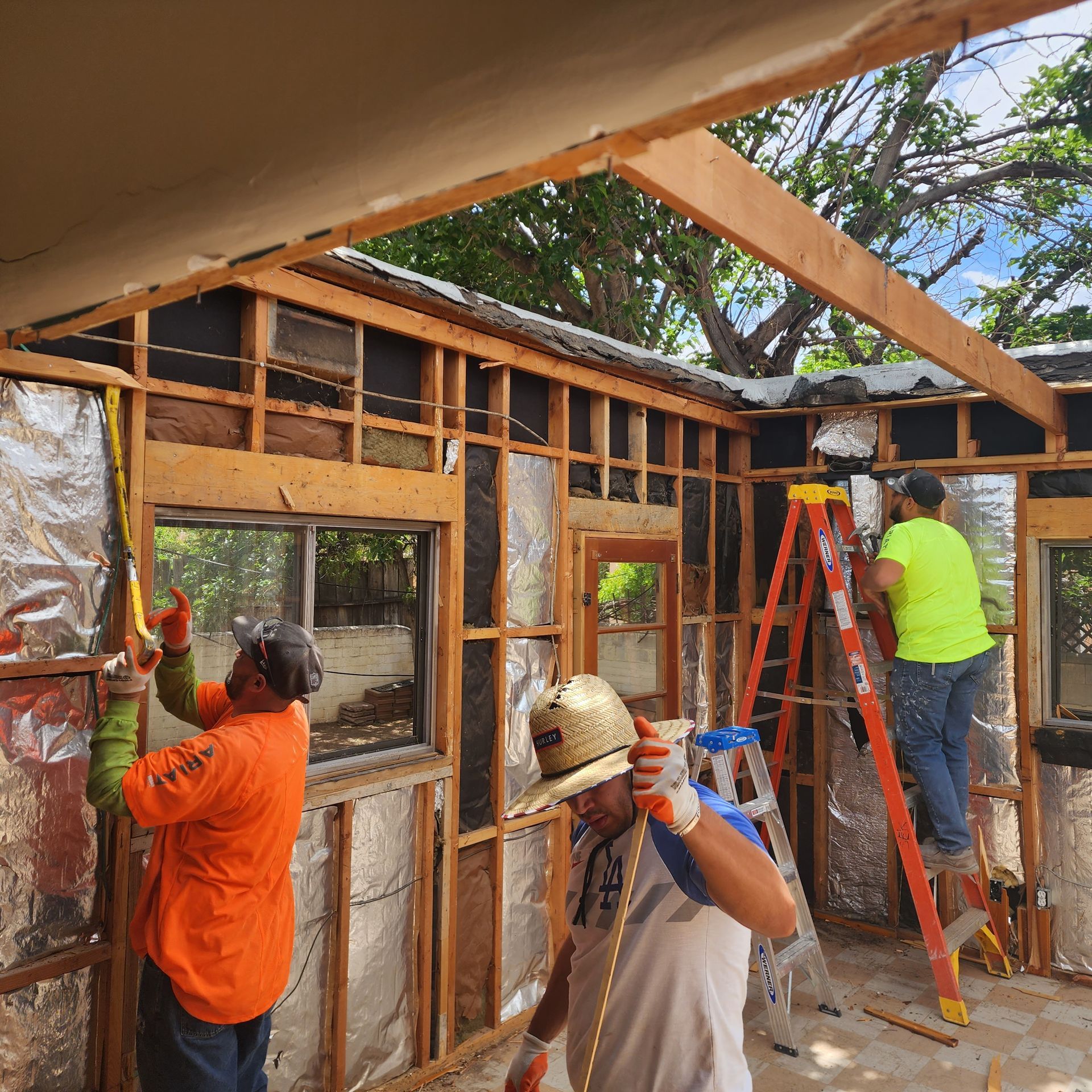 Workers framing a small structure with lumber and ladders during construction.