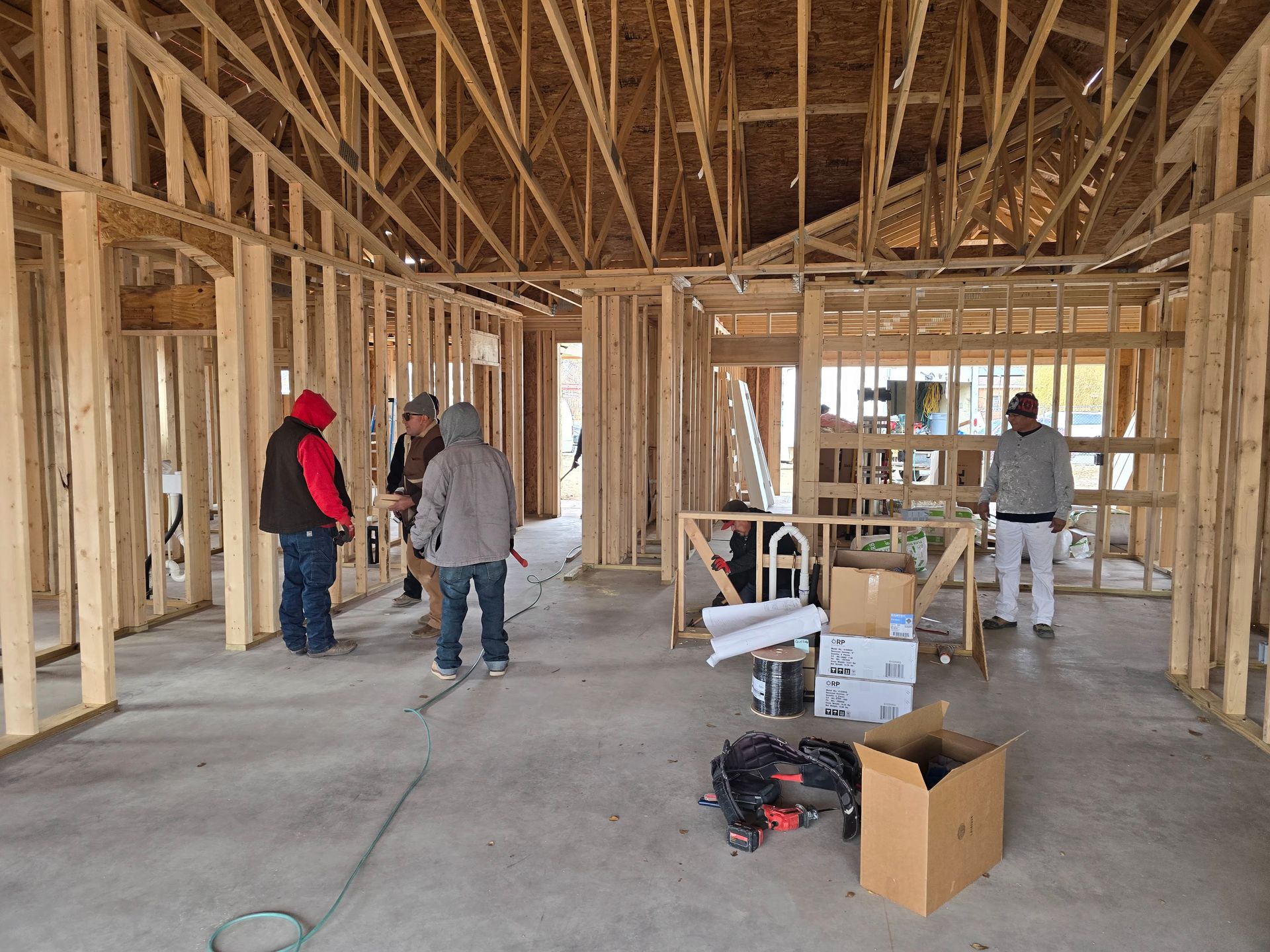 Framed house interior under construction with workers, lumber walls, exposed trusses, and tools on the floor