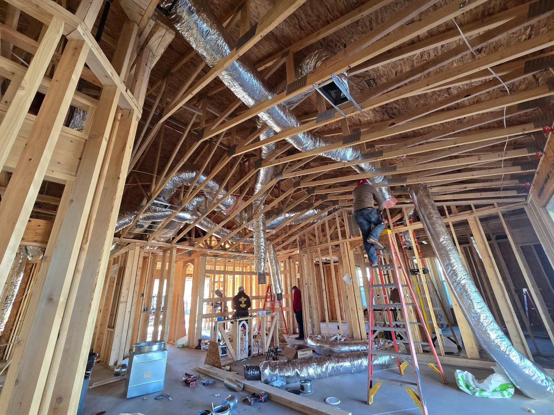 Interior of a house under construction with exposed wooden framing and two workers on ladders