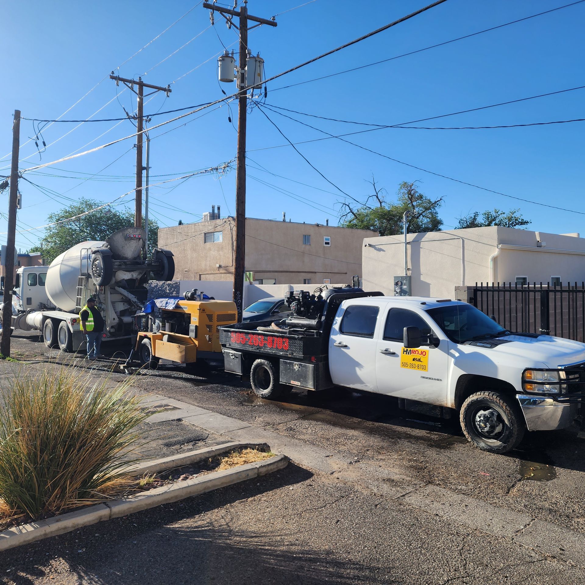 Work truck towing equipment on a street beside utility poles and a building under a clear blue sky