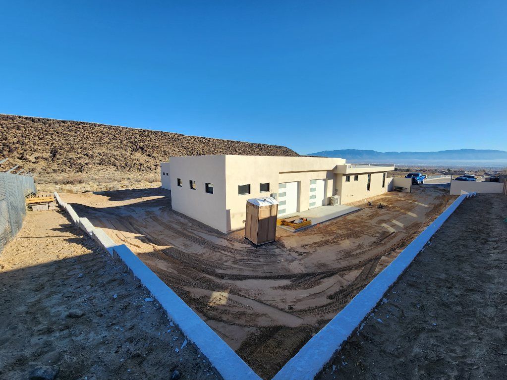 Single-story house under construction in a snowy desert landscape, with dirt paths and mountains in the background