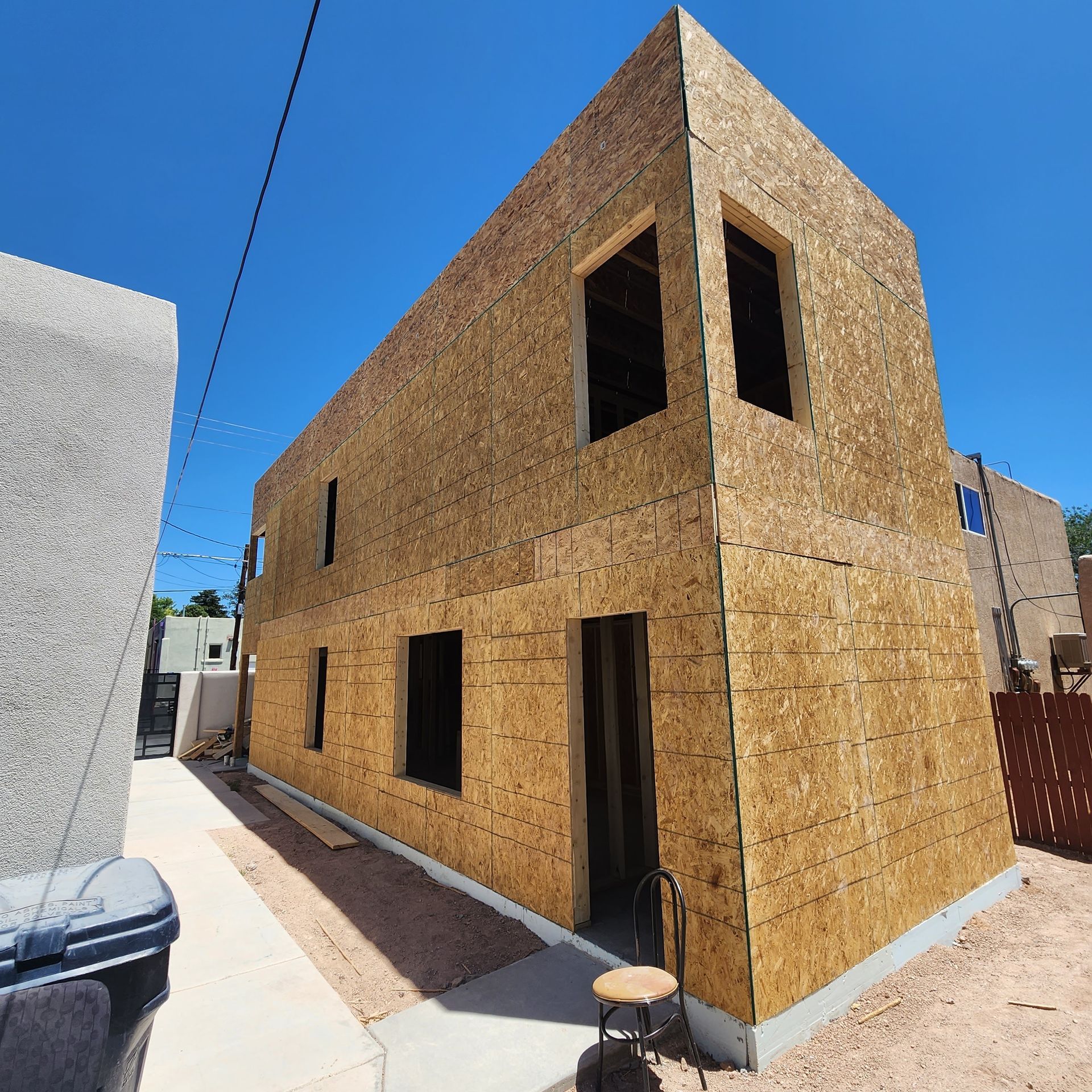 New tan stucco house under construction with black window openings along a narrow alley.