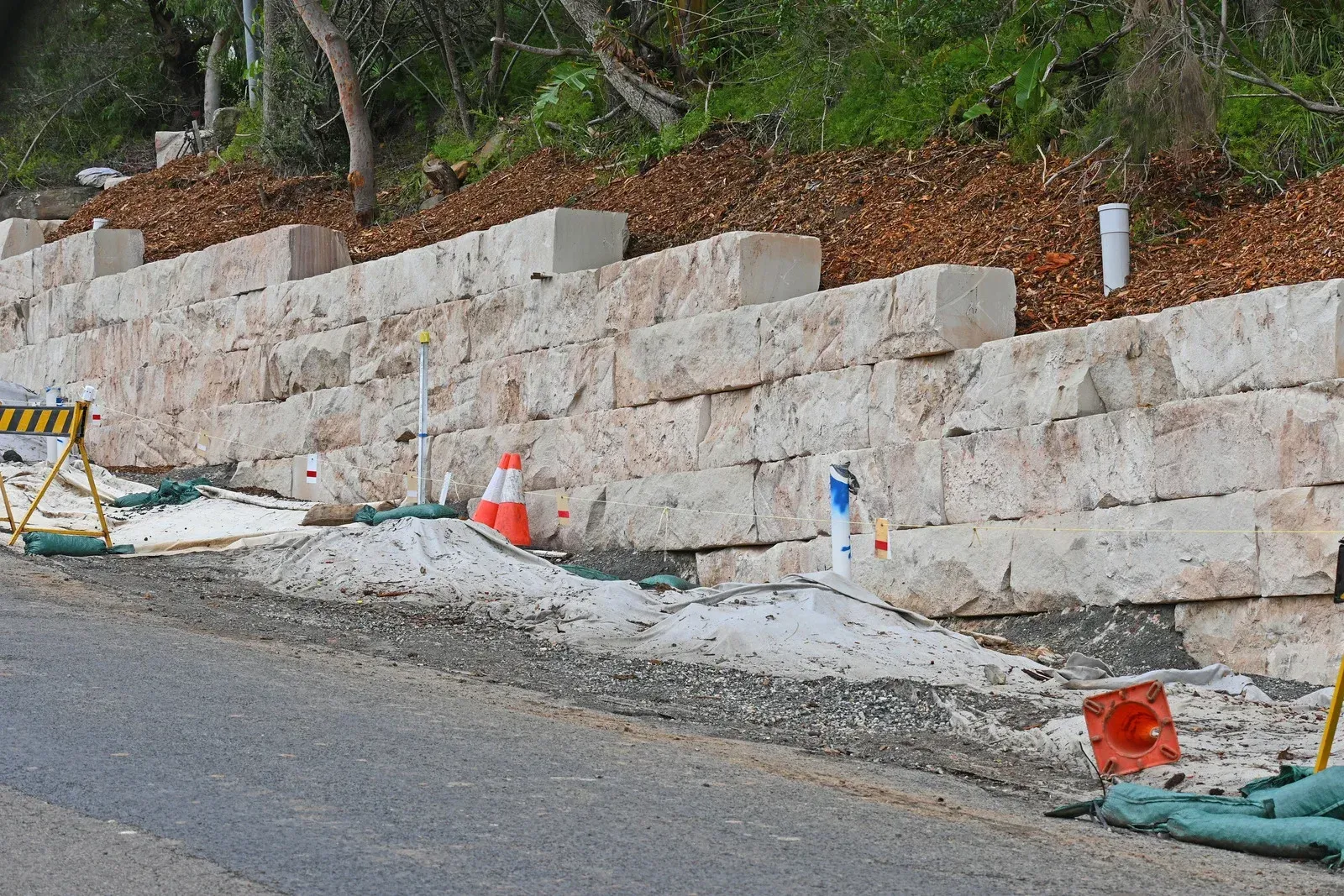 Roadside retaining wall under construction with concrete blocks, traffic cones, and construction materials