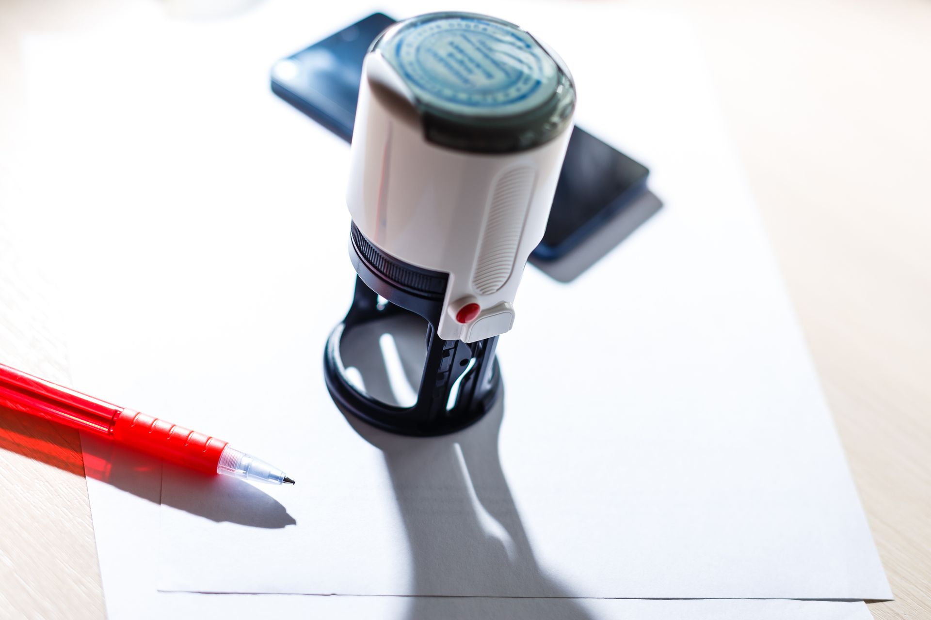 White stamp and red pen on white paper with a smartphone in the background.