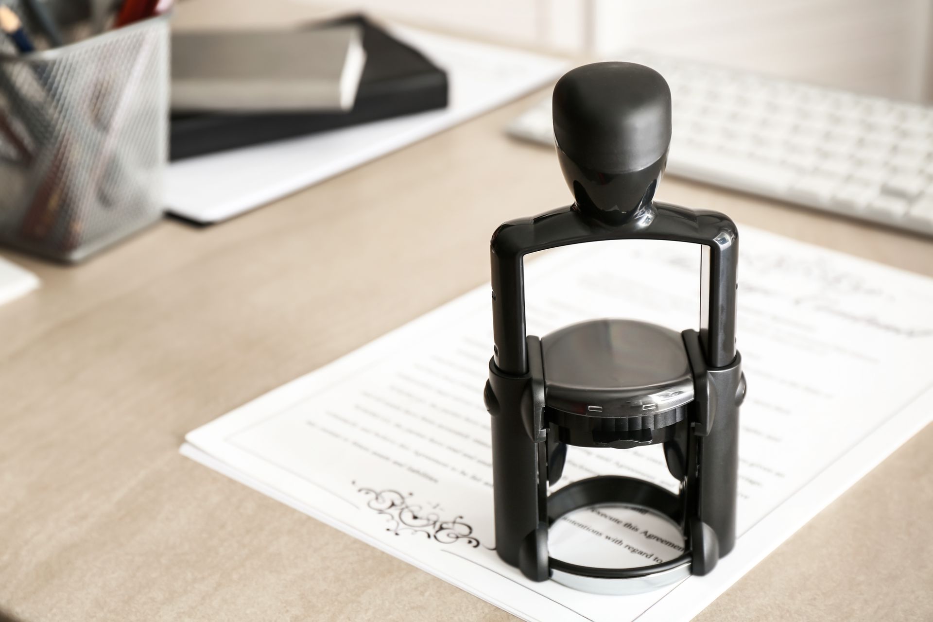 Black office stamp on white paper, keyboard and pens in background.