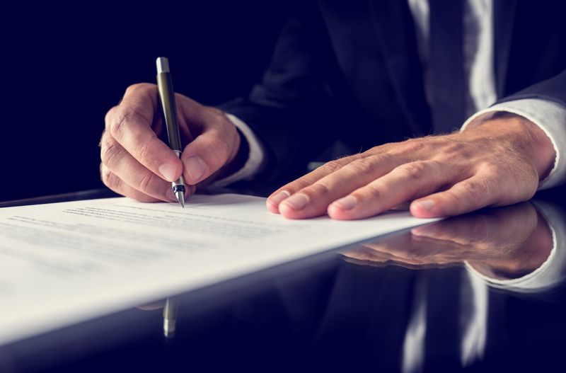A man in a suit is writing on a piece of paper with a pen.