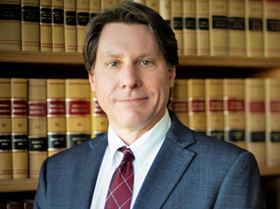 A man in a suit and tie is standing in front of a bookshelf.