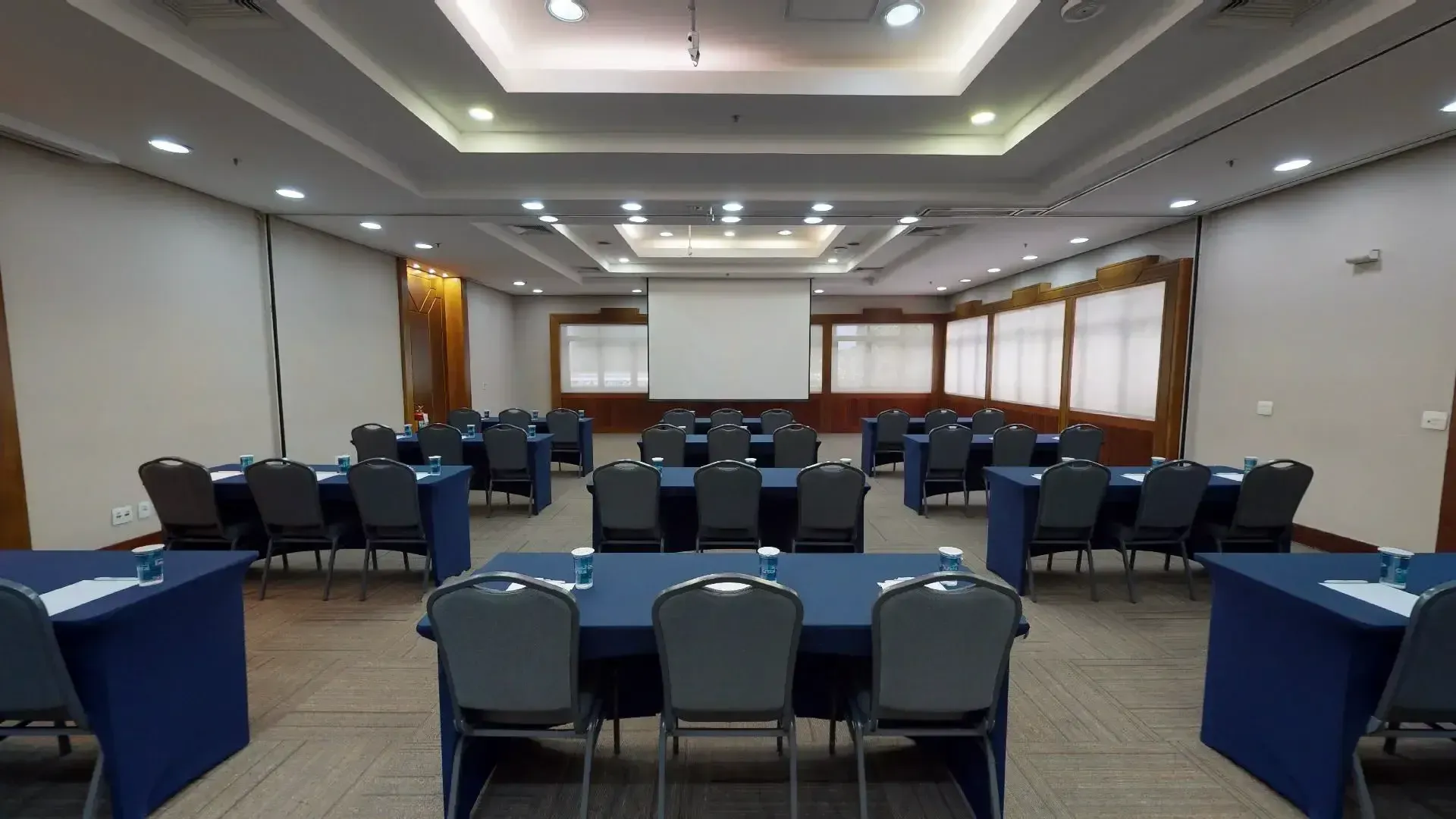 uma grande sala de conferências com mesas e cadeiras e uma tela de projeção.
