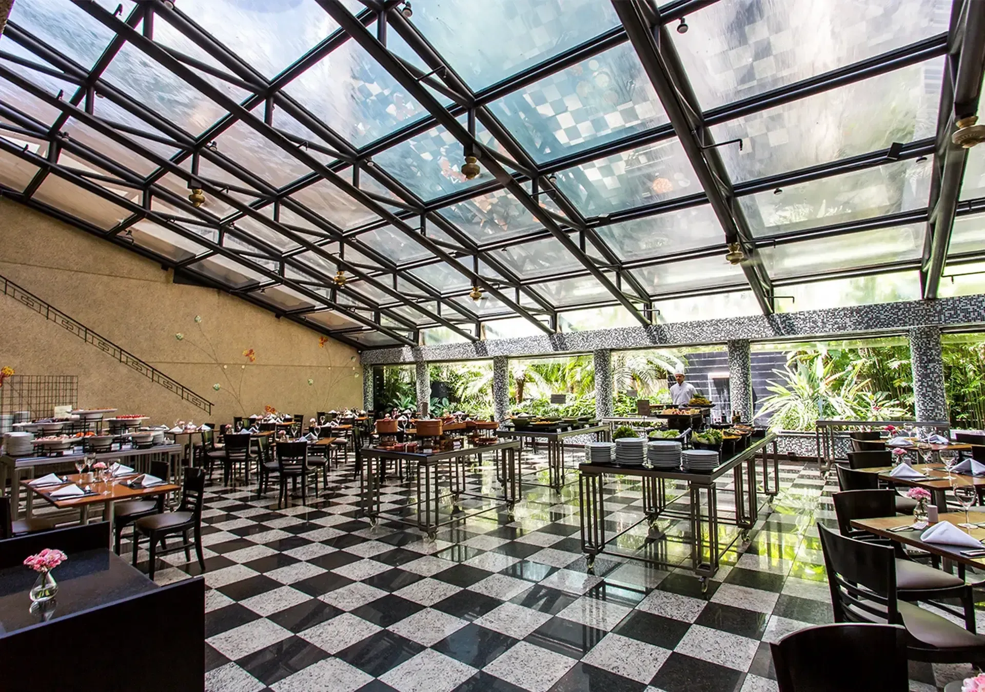 um restaurante com piso xadrez e mesas e cadeiras sob teto de vidro.