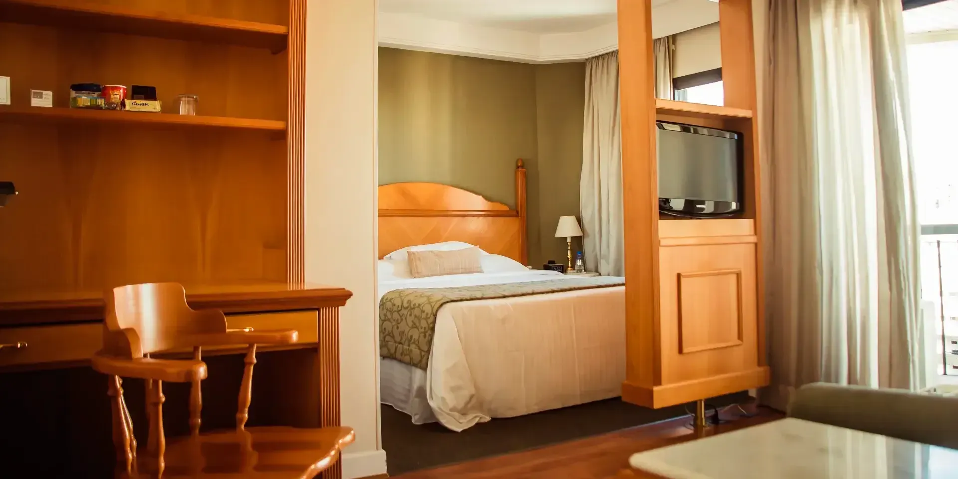 um quarto de hotel com cama, mesa, cadeira e televisão.