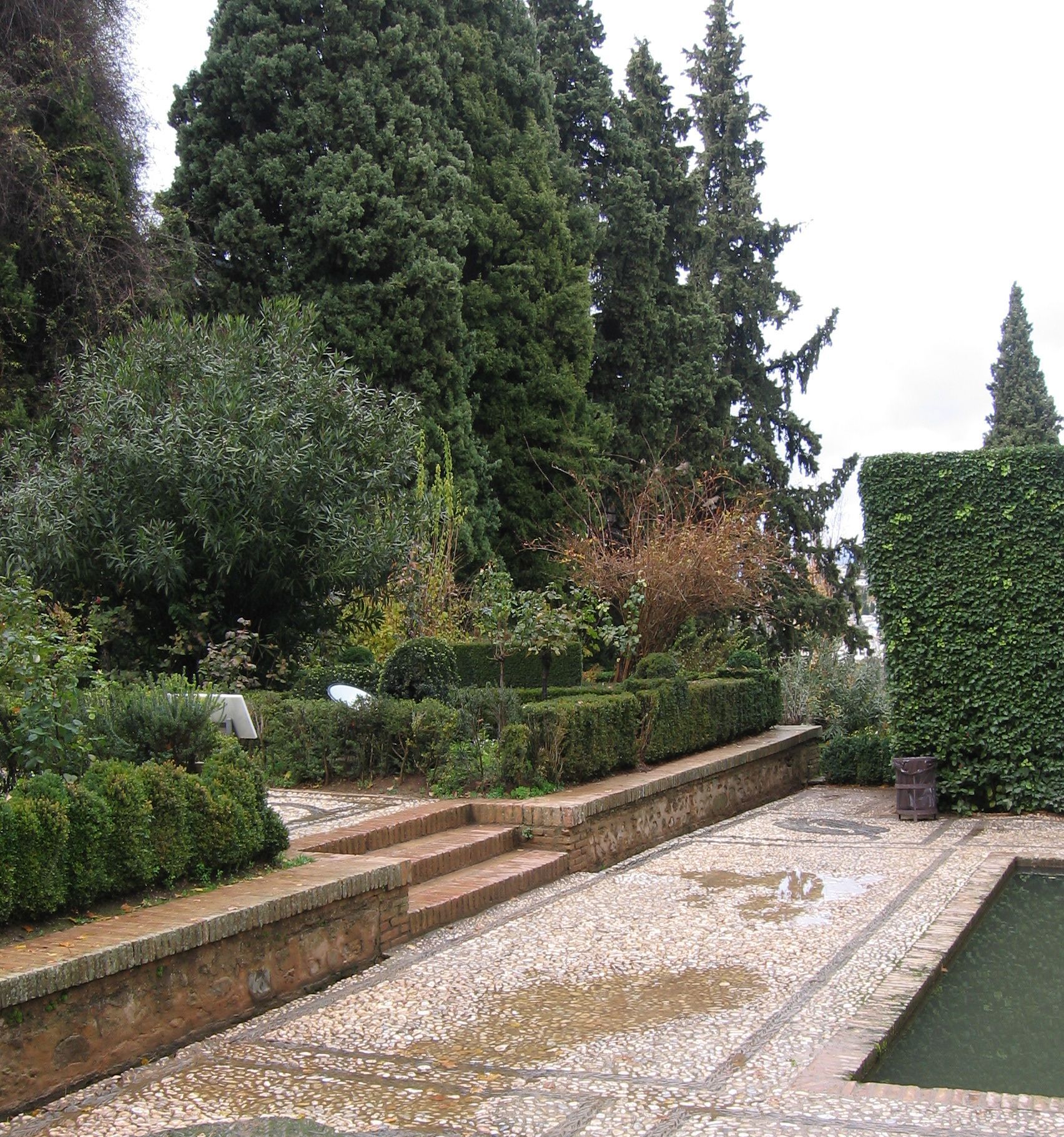 Trädgård i formell stil vid Alhambra, med många formklippa häckar och stenlagda strukturer med raka linjer.