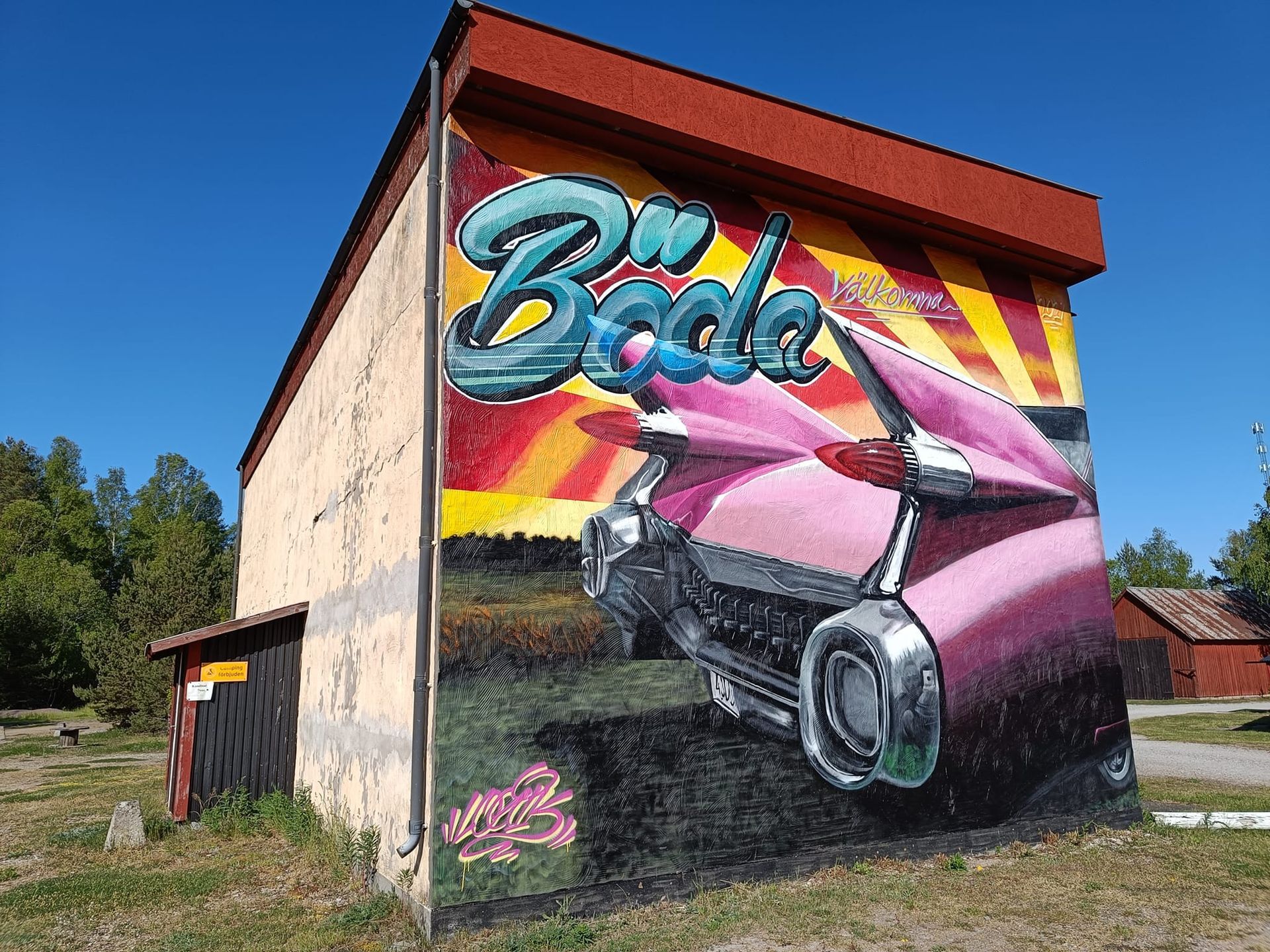 muralmålning på gammal industribyggnad som välkomnar besökare till Böda, med en rosa Cadillac