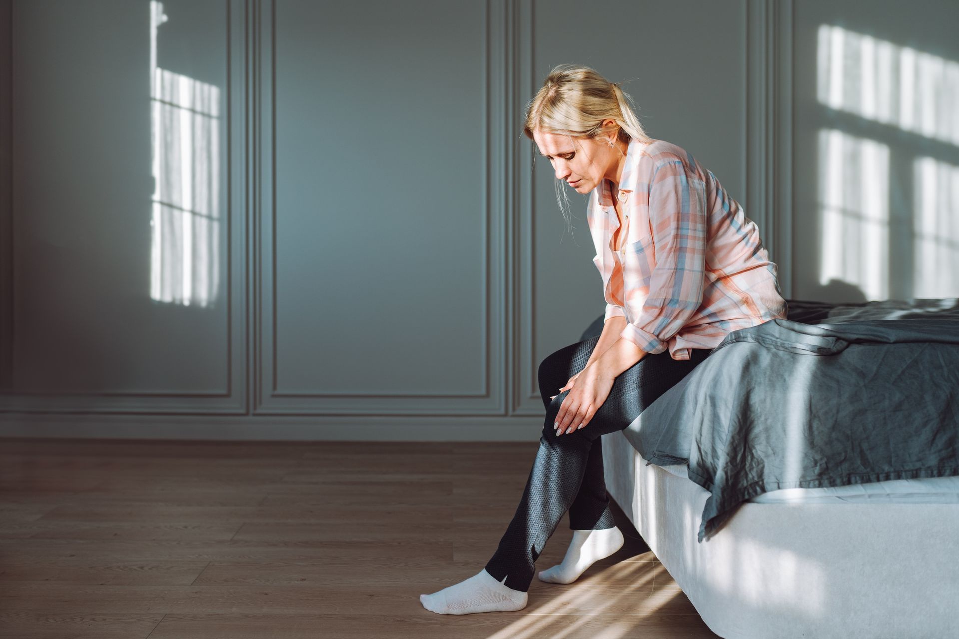 Person seated on bed gently massaging leg to ease varicose vein pain.