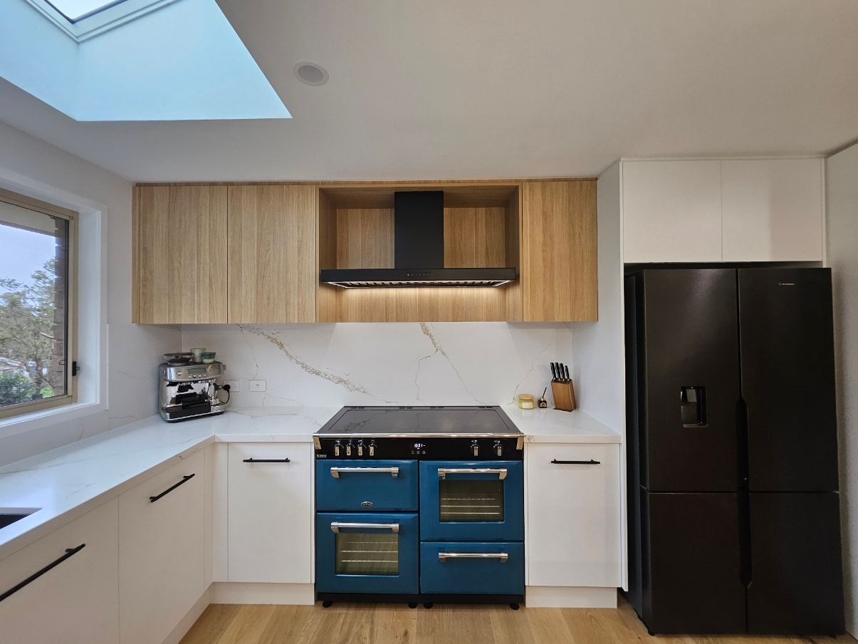 Modern Kitchen with Blue Range, Black Refrigerator, White Counters, and Wood Cabinetry Under a Skylight — JDS Kitchens & Detailed Joinery in Albion Park Rail, NSW