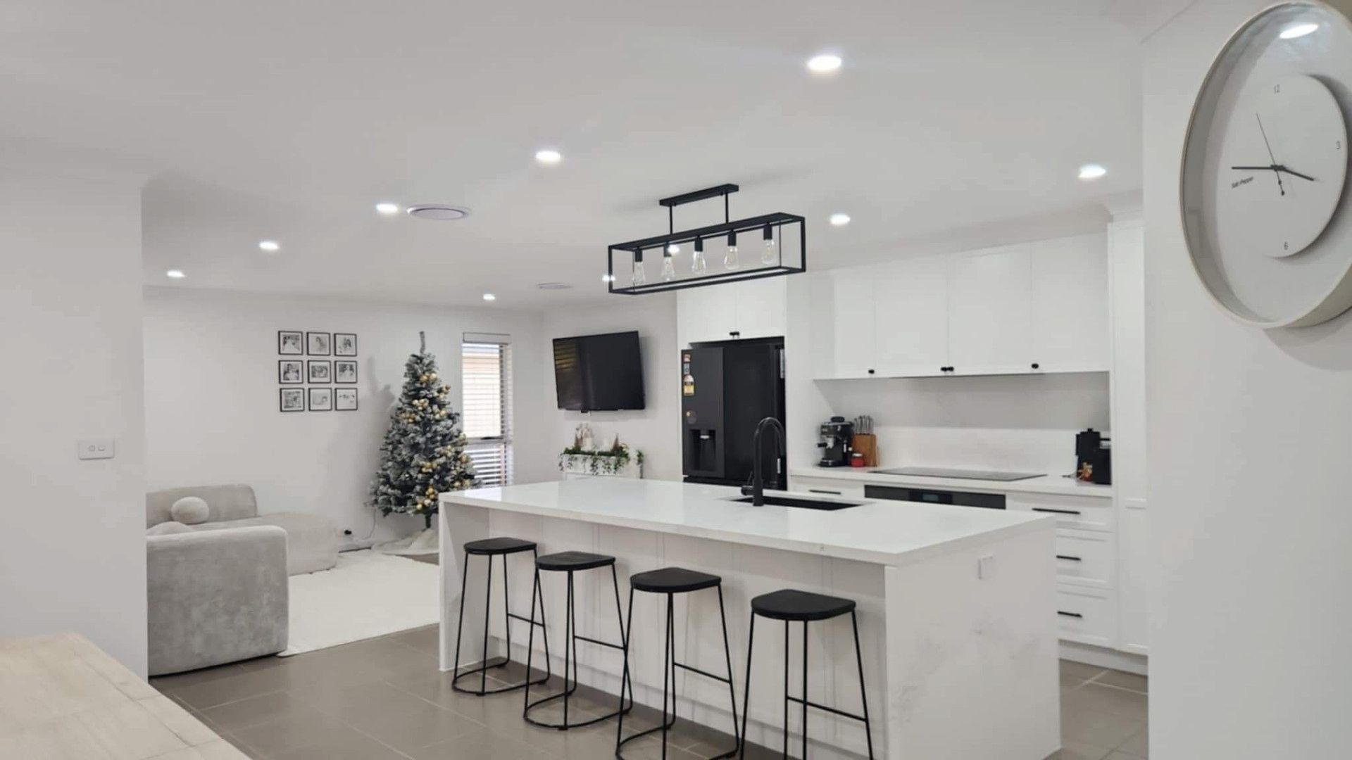Bright Modern Kitchen and Living Area with White Cabinets, Island Stools, and A Wall Clock — JDS Kitchens & Detailed Joinery in Albion Park Rail, NSW