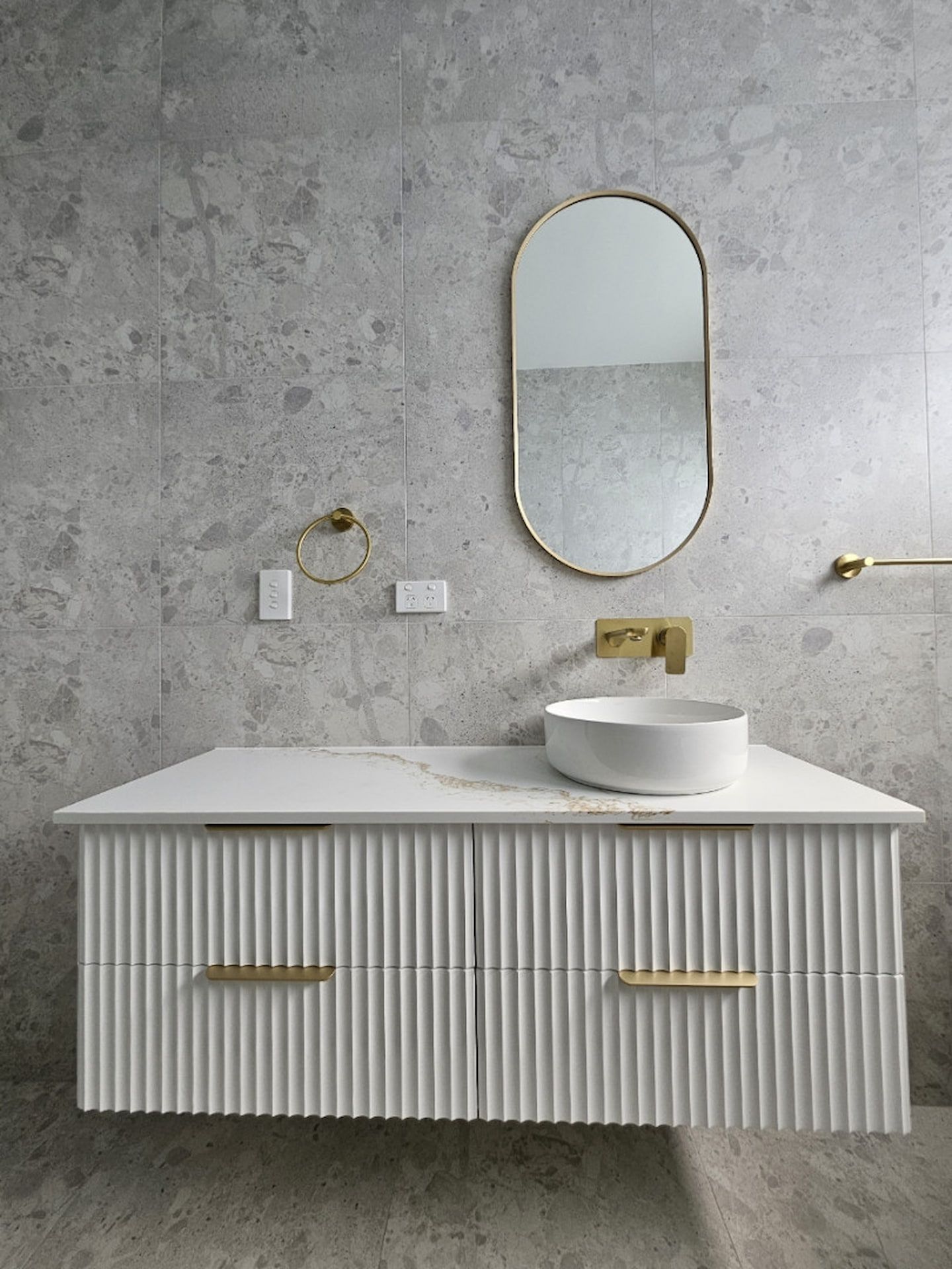 Modern Bathroom Vanity with Ribbed White Cabinet, Round Mirror, Gold Fixtures, and Stone Wall — JDS Kitchens & Detailed Joinery in Albion Park Rail, NSW