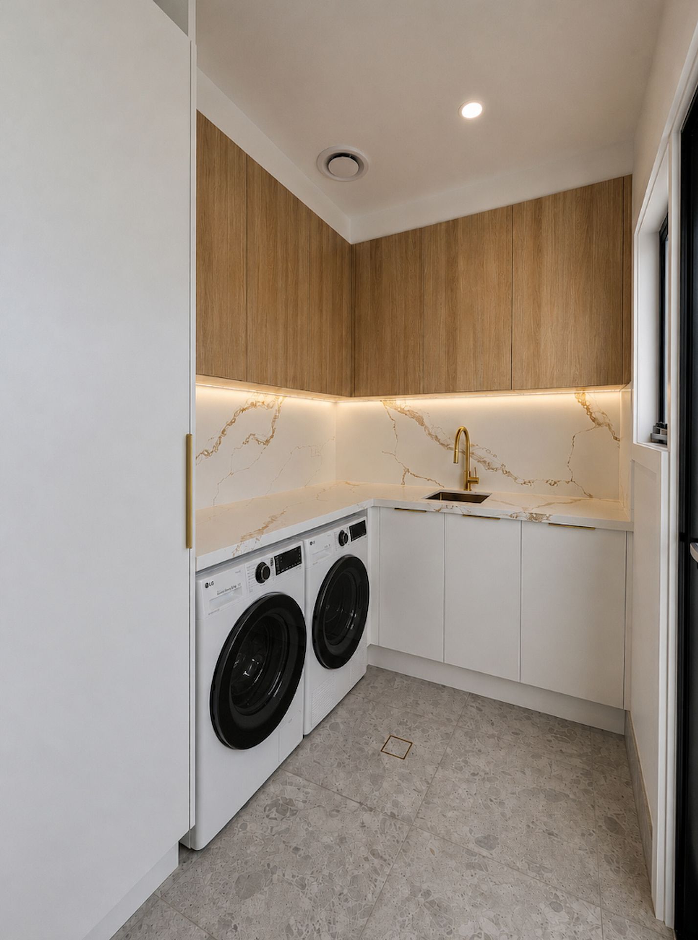 Compact Modern Laundry Room with White Cabinets, Wood Upper Panels, Marble Backsplash, and Stacked Washer Dryer — JDS Kitchens & Detailed Joinery in Albion Park Rail, NSW