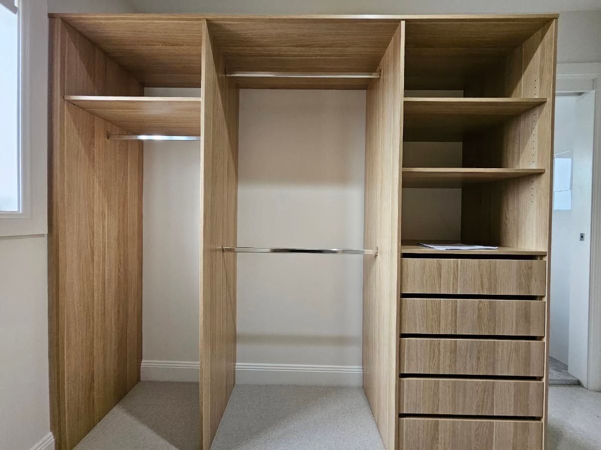 Wooden walk-in closet with shelves, hanging rods, and drawers along the right side — JDS Kitchens & Detailed Joinery in Albion Park Rail, NSW