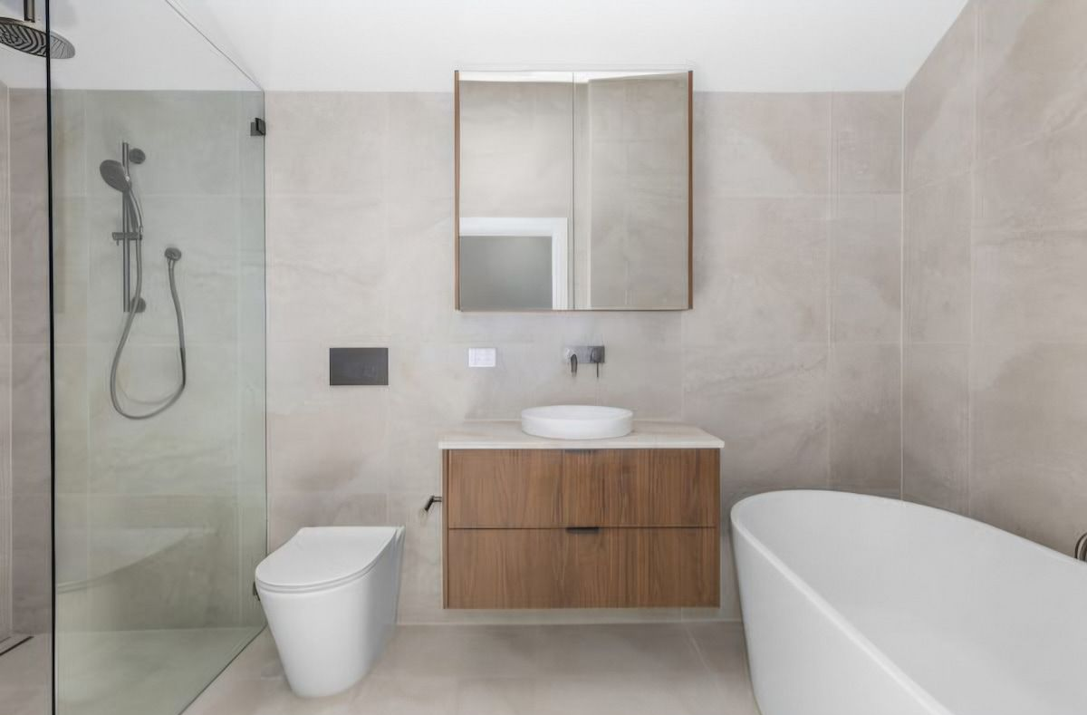 Modern bathroom with glass shower, wall-mounted toilet, wood vanity, and white bathtub — JDS Kitchens & Detailed Joinery in Albion Park Rail, NSW