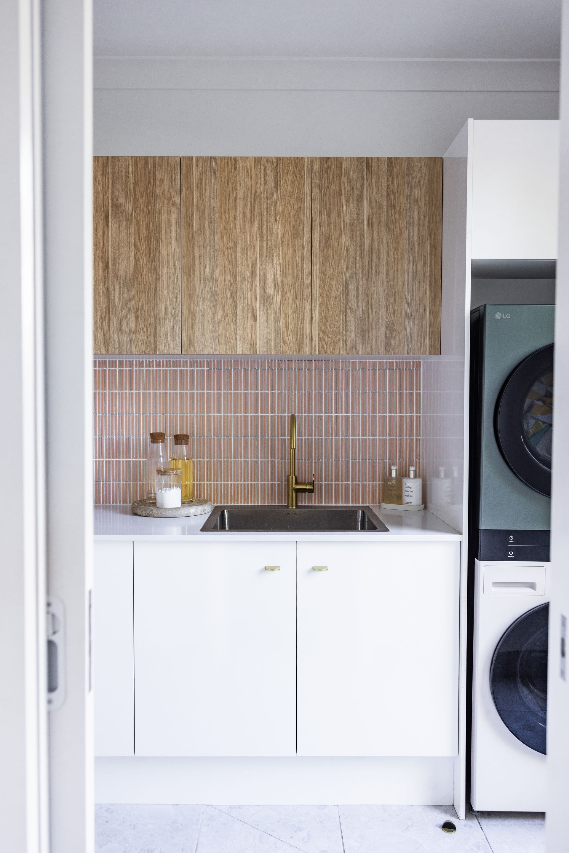 Small Laundry Nook with White Sink Cabinet, Pink Tile Backsplash, Wood Upper Cabinets, and A Stacked Washer-Dryer — JDS Kitchens & Detailed Joinery in Albion Park Rail, NSW