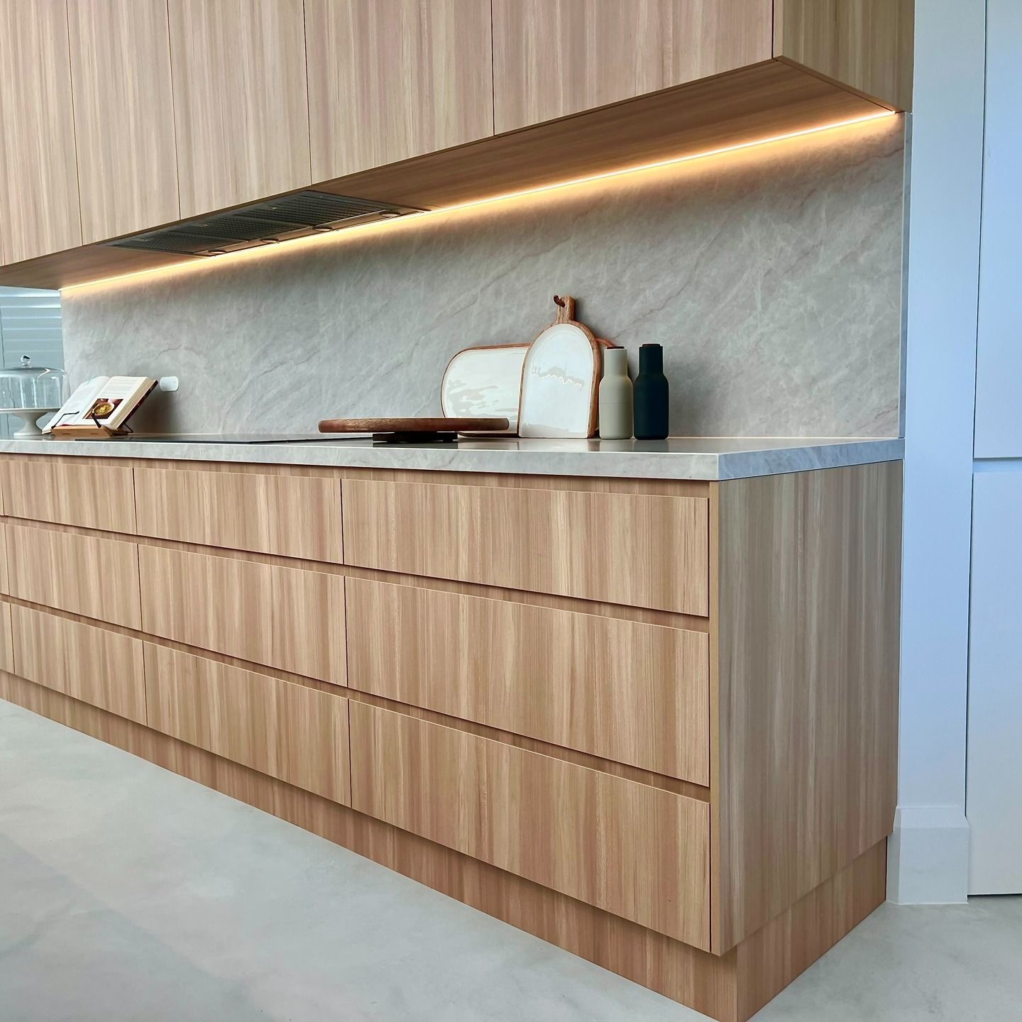 Modern minimalist wooden reception desk with warm under-shelf lighting and a light stone backdrop — JDS Kitchens & Detailed Joinery in Albion Park Rail, NSW