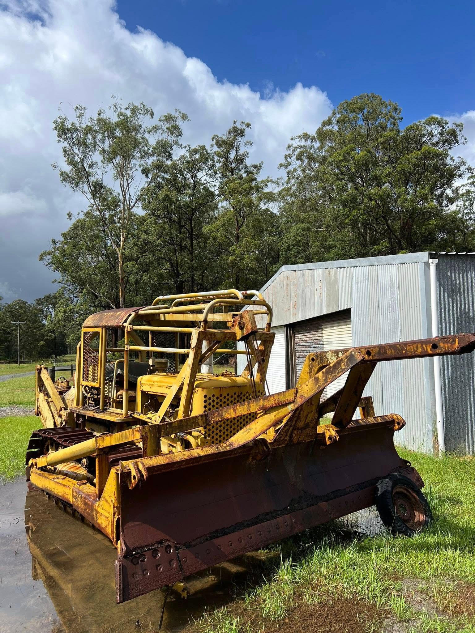 Rusty Yellow Bulldozer Parked Beside a White Metal Shed on Grass Under a Blue Sky — North Coast Heavy Diesel In Wauchope, NSW