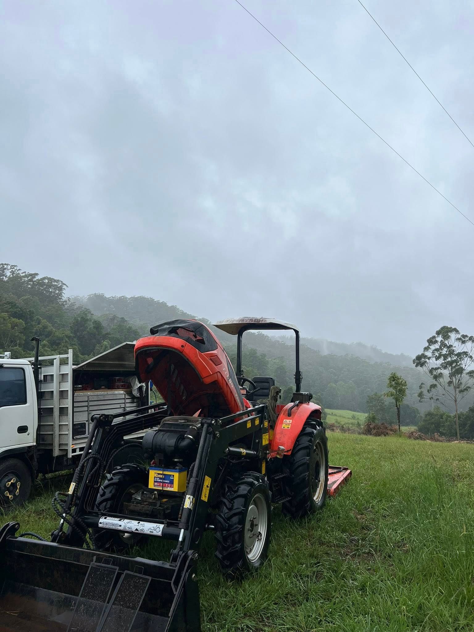 Orange Tractor With Front Loader on Wet Grass in Rainy Field — North Coast Heavy Diesel In Macksville, NSW