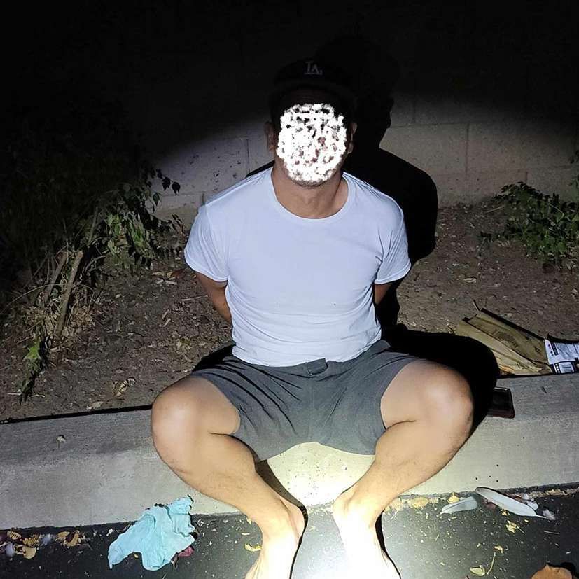 A man in a white shirt and shorts is sitting on a curb at night.