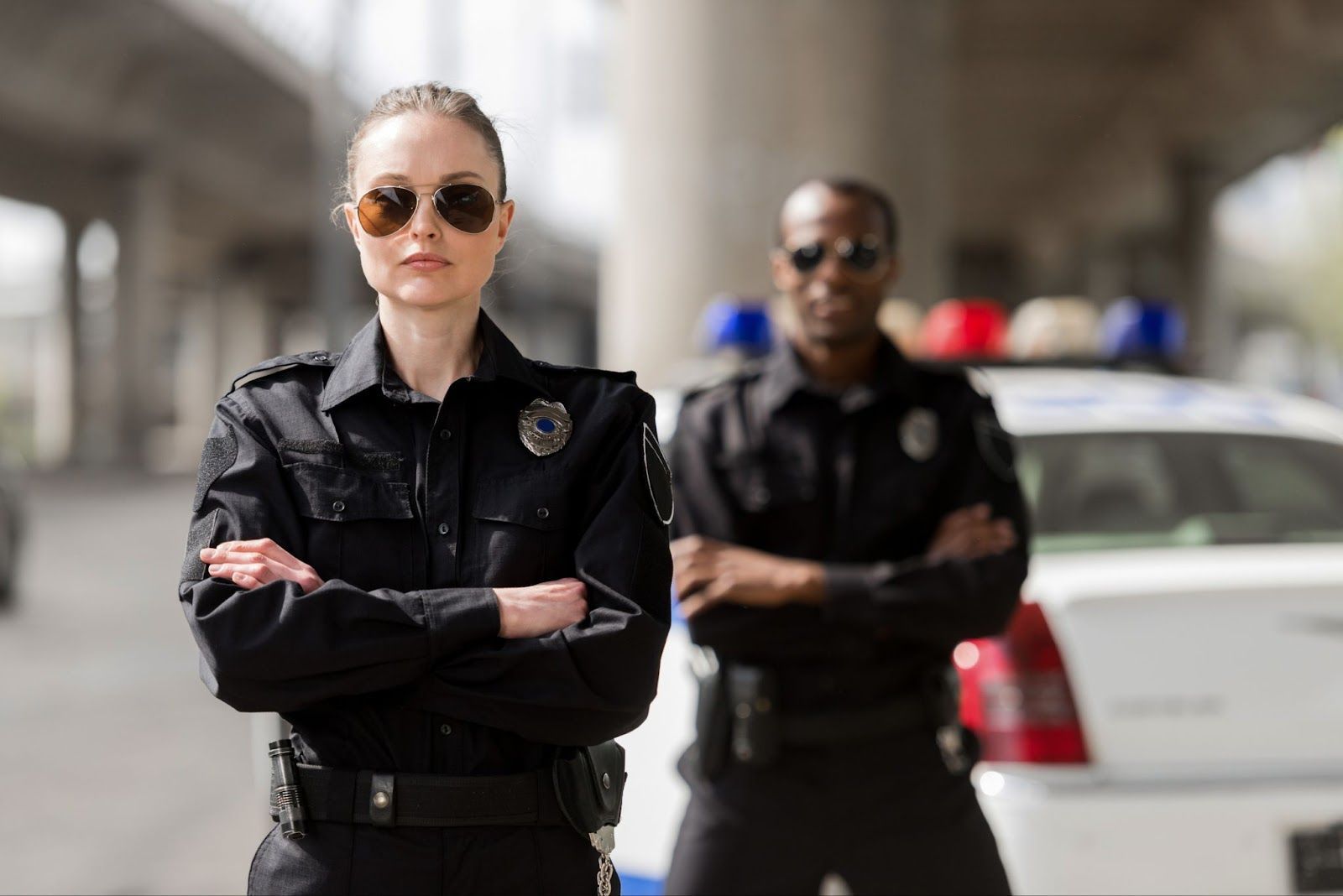 A man and a woman are standing next to each other in front of a police car.
