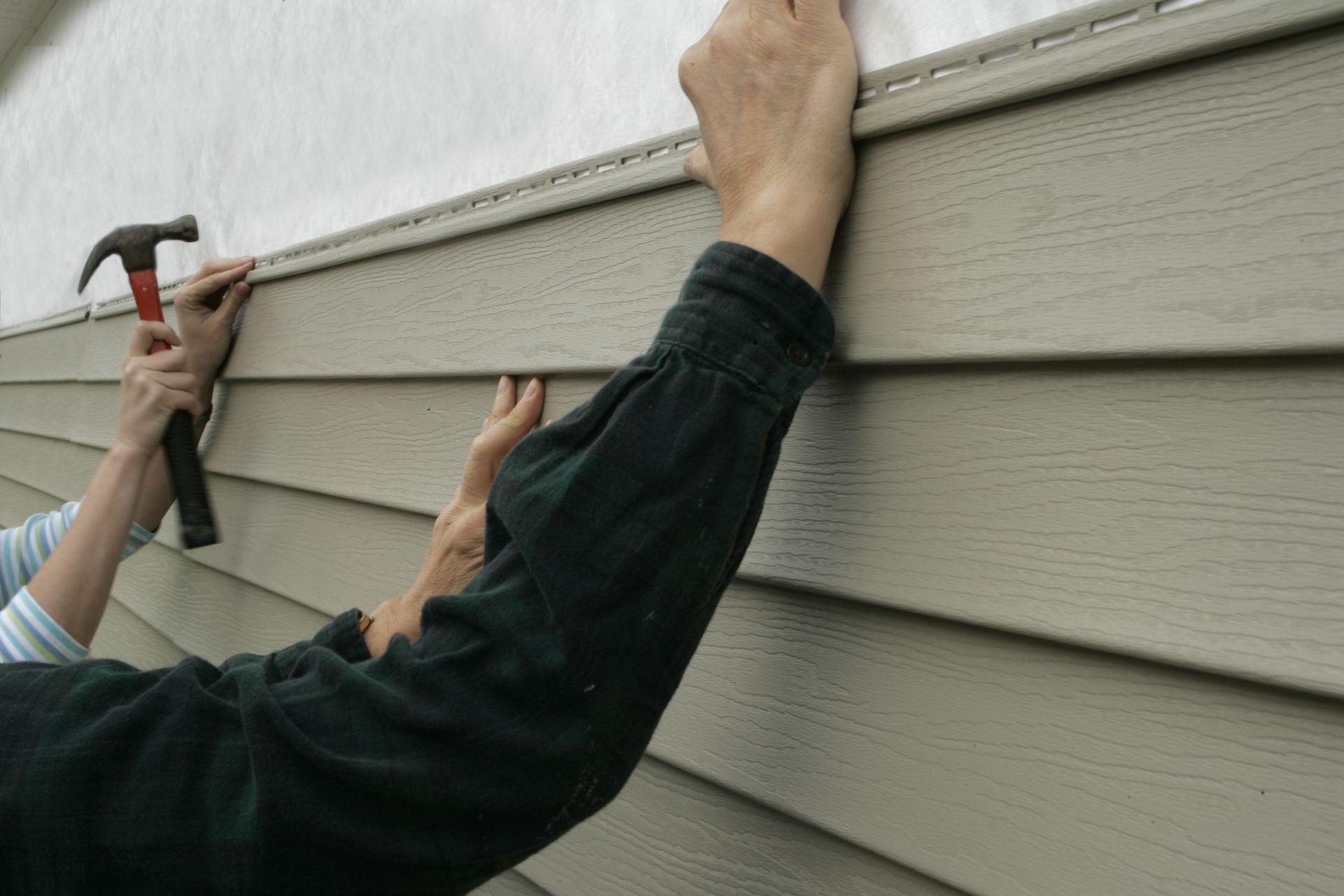 Person hammering siding while holding it in place on a house exterior